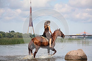Beautiful teenage girl riding horse in the river