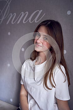 a beautiful teenage girl sits on a bed near the wall with her name written on it