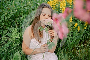 Beautiful teenage girl sits in a blooming garden, with a flower in her hand