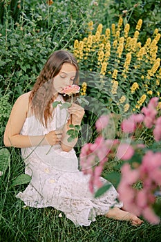 Beautiful teenage girl sits in a blooming garden, with a flower in her hand