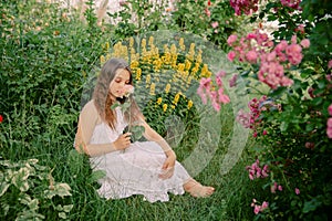 Beautiful teenage girl sits in a blooming garden, with a flower in her hand