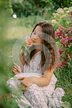 Beautiful teenage girl sits in a blooming garden, with a flower in her hand