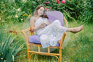 Beautiful teenage girl sitting on a chair in the garden with flowers