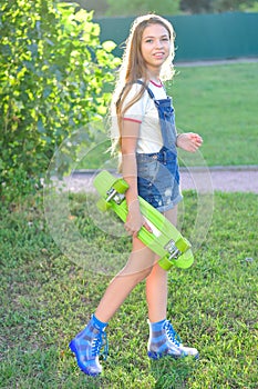 Beautiful teenage girl with skateboard in the green park in summer