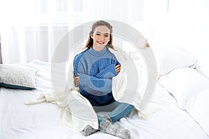 Beautiful teenage girl in warm cozy sweater with plaid sitting on bed