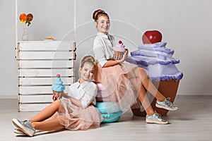 Beautiful teenage girls in pink tutu skirts with lollipops and macaroons and fansy cakes in studio on white background