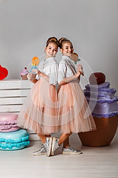 Beautiful teenage girls in pink tutu skirts with lollipops and macaroons and fansy cakes in studio on white background