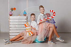 Beautiful teenage girls in pink tutu skirts with lollipops and macaroons and fansy cakes in studio on white background