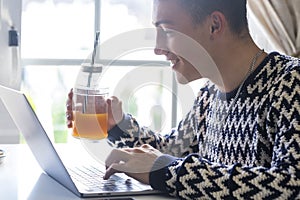 Beautiful teenager drinking an orange juice using laptop at home in front of the window -  Millenial generation enjoying