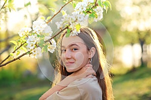 Beautiful teenager girl with blooming apple flowers. Happy cute kid having fun outdoors at sunset