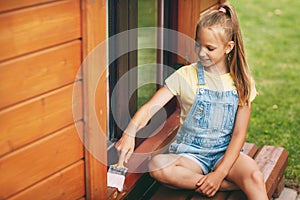 Beautiful teenager girl in denim overalls and a yellow T-shirt holds a brush in her hands and smiles. Happy family. Home