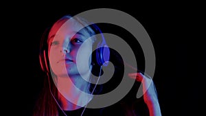 Beautiful teenager girl listening music headphones in dark room with neon lighting. Relaxing girl enjoying music in