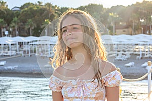 Beautiful teenager girl in the rays of the setting sun on a pier by the sea