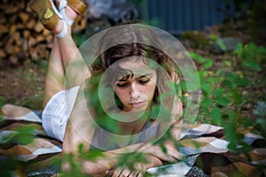 Beautiful teenager girl reading a book lying on blanket on green grass at the forest