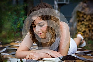 Beautiful teenager girl reading a book lying on blanket on green grass at the forest