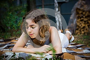 Beautiful teenager girl reading a book lying on blanket on green grass at the forest