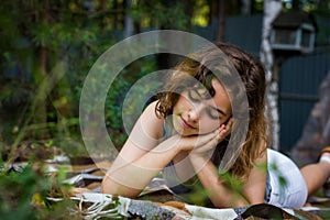 Beautiful teenager girl reading a book lying on blanket on green grass at the forest