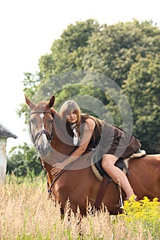 Beautiful teenager girl riding horse at the field of flowers
