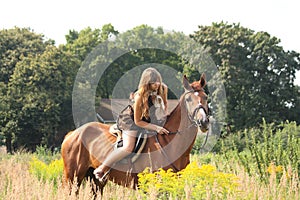 Beautiful teenager girl riding horse at the field of flowers