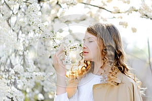 Beautiful teenager girl girl smelling flowers and enjoying warm sunny spring weather at countryside