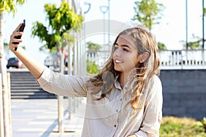 Beautiful teenager girl taking a selfie on the promenade on a sunny day. Happy young girl smiling with a phone in her hands