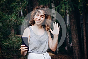 Beautiful teenager girl talking with friends by video call at the forest. Girl taking a selfie