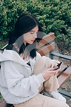 Beautiful teenager girl using smartphone while sitting alone on the bench outdoor