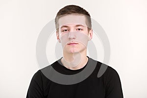 A beautiful teenager man with a serious sad face, dark hair and a black T-shirt with hands folded on a white background. Mock up,