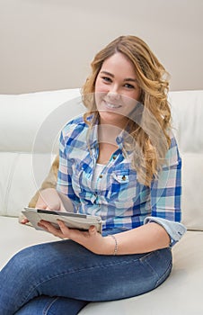 Beautiful teenager using tablet pc sitting on sofa