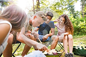 Teenagers camping, cooking vegetables on barbecue grill.