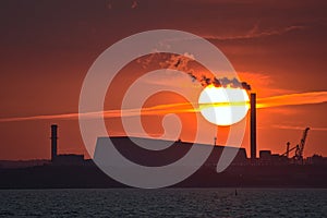 Beautiful telephoto view of epic orange sunset over Dublin port and Sun aligned with Covanta Plant Dublin Waste to Energy