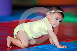 Beautiful ten months baby girl crawling on a colorful background. Early stimulation for toddlers concept