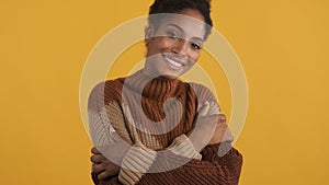 Beautiful tender african american girl in cozy knitted sweater happily enjoying warm looking in camera over yellow photo