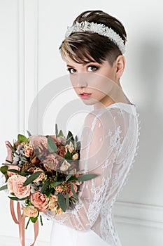 Beautiful tender bride girl with short haircut with crown on head with bouquet of flowers and elegant wedding dress