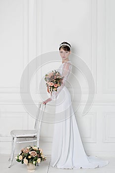 Beautiful tender elegant young girl bride in wedding dress with crown on head in studio on white background with bouquet in hands