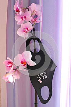 End of pandemic. Beautiful tender flowers of pink orchid with black pitta mask.