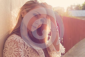 Beautiful tender girl near the wall , next to a wooden fence at sunset in the city, volntse hair