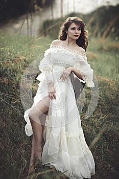 A beautiful tender girl in a white dress sits on a tree stump.