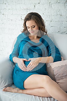 Beautiful tender pregnant woman sit on a sofa