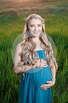 Beautiful tender pregnant woman standing on green grass