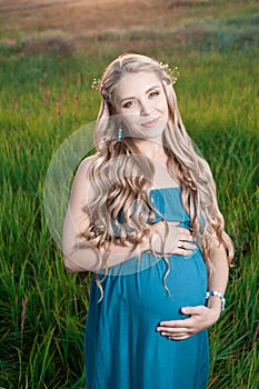 Beautiful tender pregnant woman standing on green grass