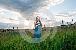 Beautiful tender pregnant woman standing on green grass