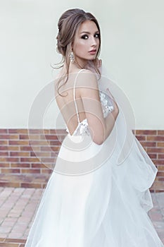 Beautiful tender sweet girl bride with a festive hairdo and light make-up with a veil in her hands with rich costume jewelery earr