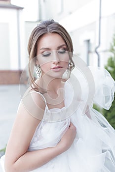 Beautiful tender sweet girl bride with a festive hairdo and light make-up with a veil in her hands with rich costume jewelery earr