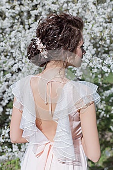 Beautiful tender sweet girl in a pink dress with a hairdo near blossoming tree on a sunny spring day