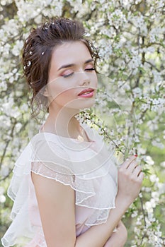 Beautiful tender sweet girl in a pink dress with a hairdo near blossoming tree on a sunny spring day