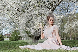 Beautiful tender sweet girl in a pink dress with a hairdo near blossoming tree on a sunny spring day