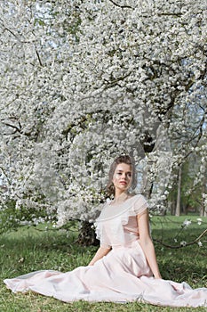 Beautiful tender sweet girl in a pink dress with a hairdo near blossoming tree on a sunny spring day