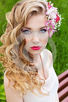 Beautiful tender sweet girl in a white dress with a wedding hairdo curls bright makeup and red lips with flowers in her hair