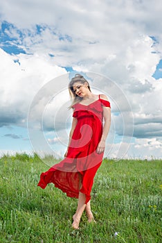 Beautiful tender woman in red dress stand on green grass